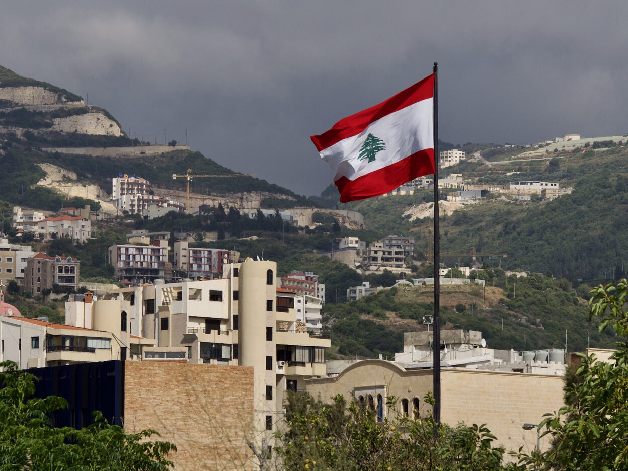 The Lebanese flag waving in the wind near Byblos, with mountains in the background