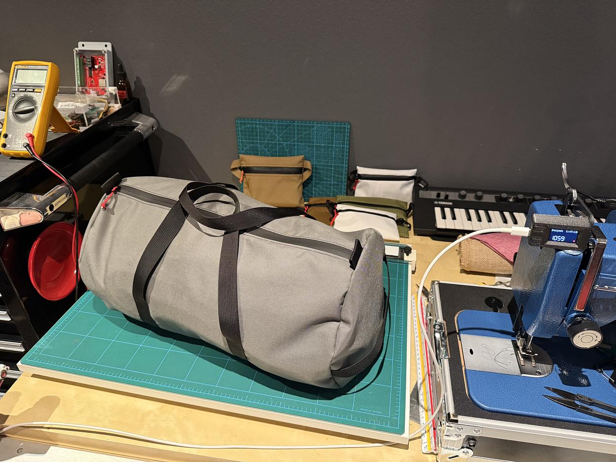 A light grey duffel bag with black straps, made by Zef Houssney